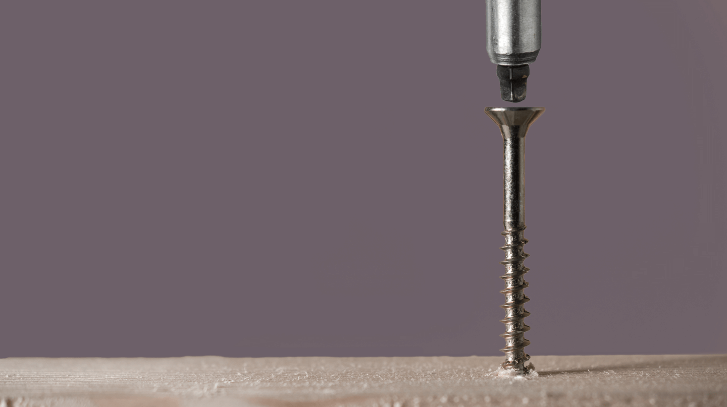 A close up of a drill bit drilling a screw into a piece of wood